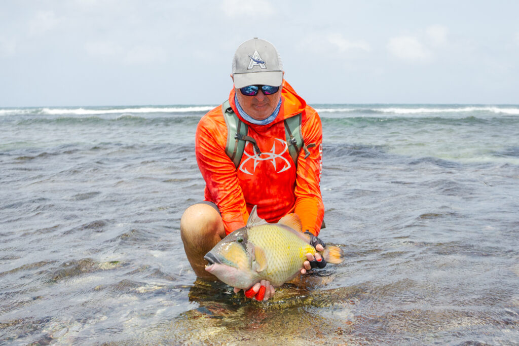 Angler in organge jacket releasing a triggerfish